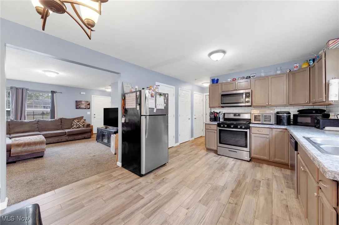 Kitchen featuring appliances with stainless steel finishes, light countertops, light wood finished floors, open floor plan, and tasteful backsplash