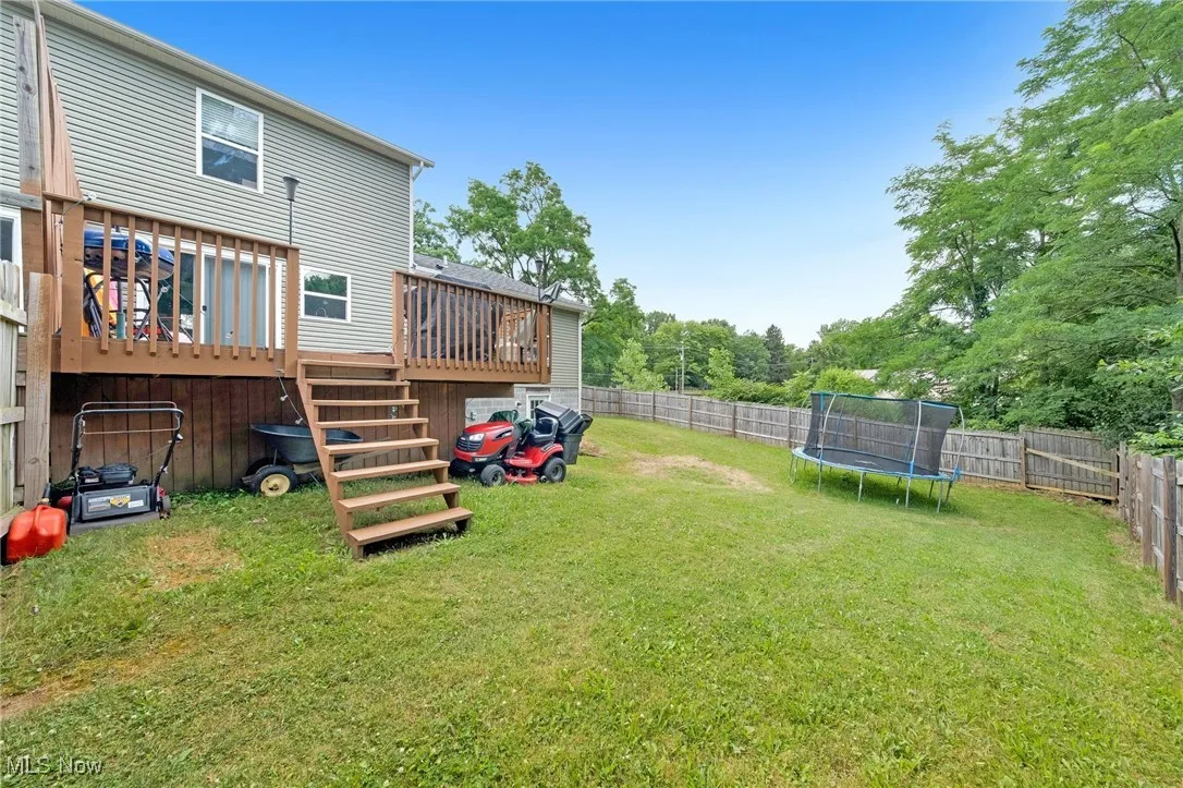 Fenced backyard featuring a trampoline, a wooden deck, and stairway