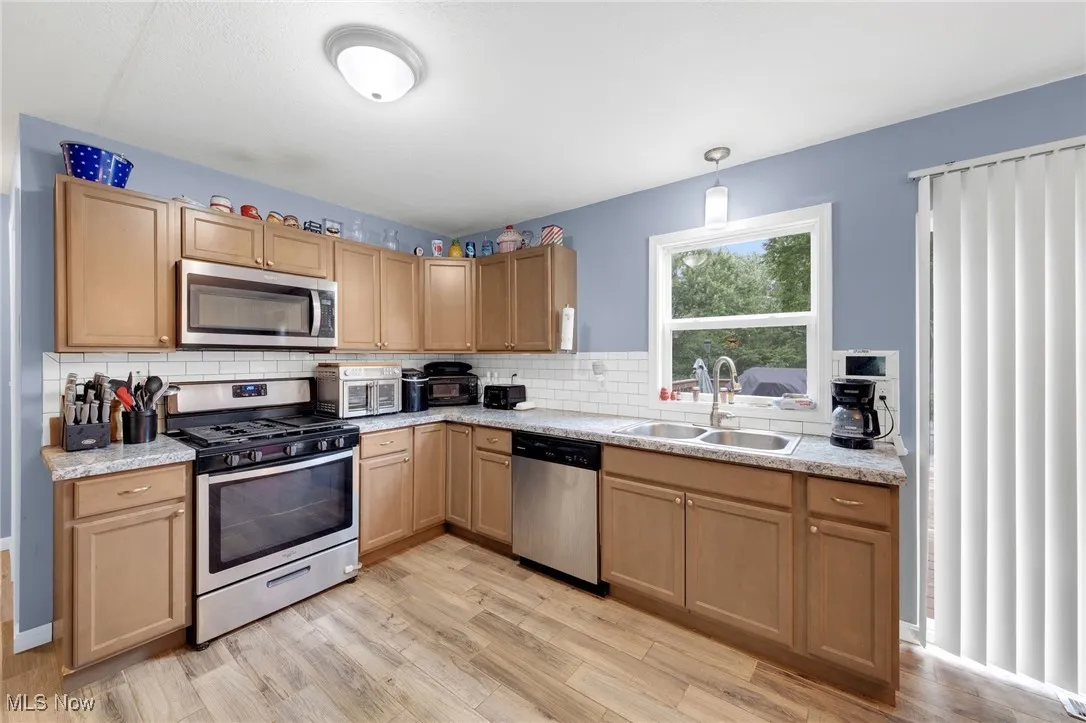 Kitchen with appliances with stainless steel finishes, light countertops, light wood finished floors, and backsplash