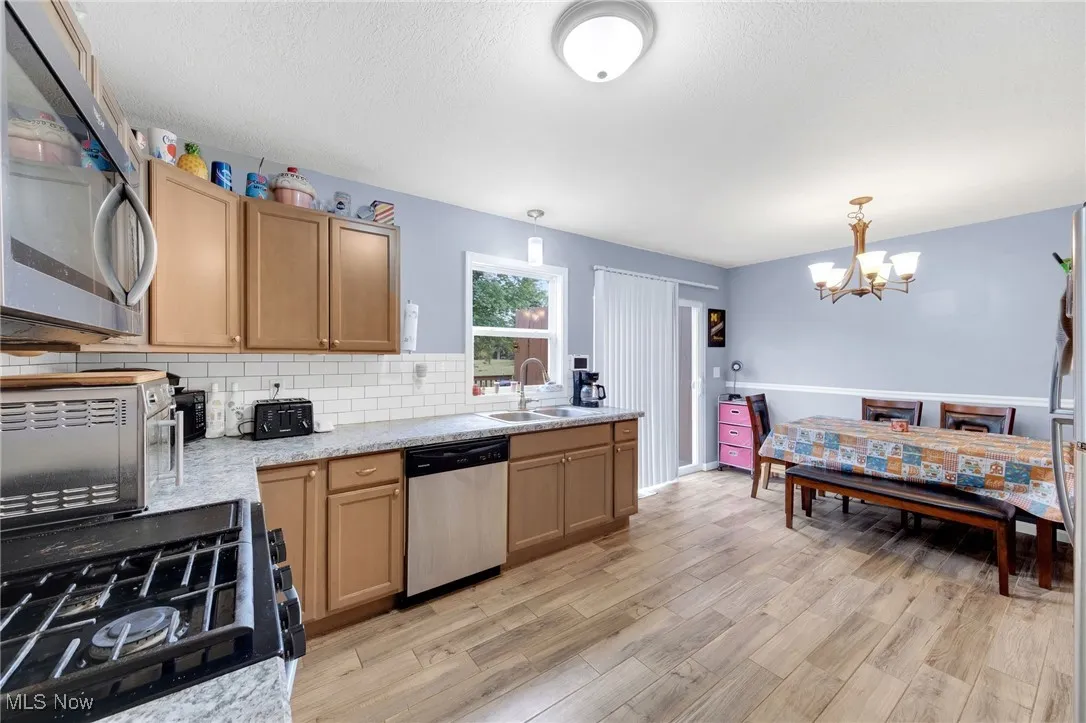 Kitchen featuring stainless steel appliances, a chandelier, backsplash, light wood-style flooring, and pendant lighting