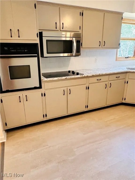 Kitchen featuring white oven, stainless steel microwave, decorative backsplash, black electric cooktop, and light stone counters