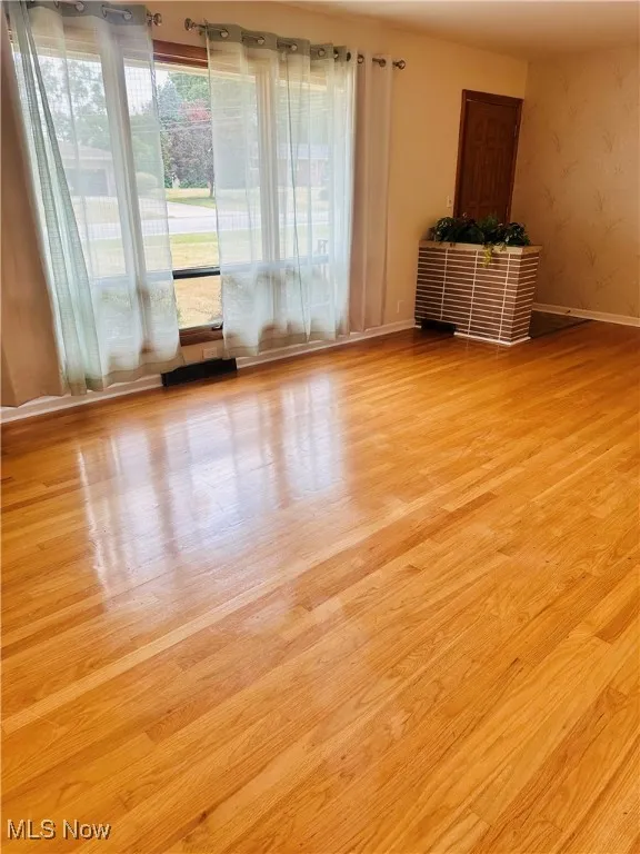 Unfurnished room featuring wood finished floors and wallpapered walls