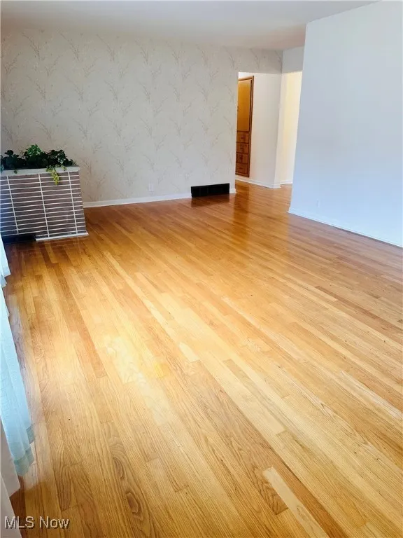 Unfurnished room featuring wallpapered walls and wood finished floors