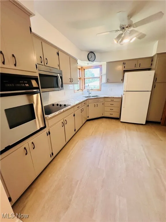 Kitchen featuring stainless steel appliances, backsplash, light countertops, a ceiling fan, and light wood-type flooring
