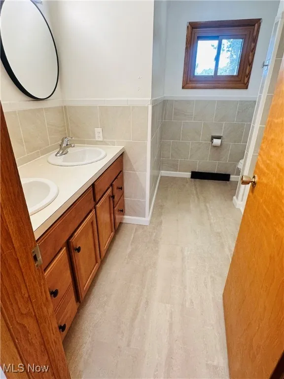 Bathroom with tile walls, double vanity, and a wainscoted wall