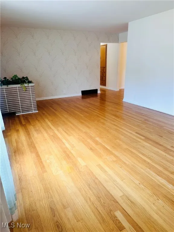 Spare room featuring wallpapered walls and wood finished floors