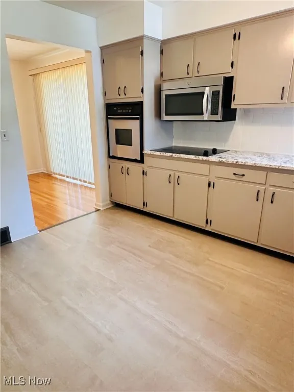 Kitchen with backsplash, stainless steel appliances, light wood-style flooring, and cream cabinets