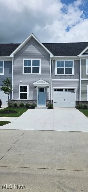 View of front of home with concrete driveway, a garage, board and batten siding, roof with shingles, and stone siding