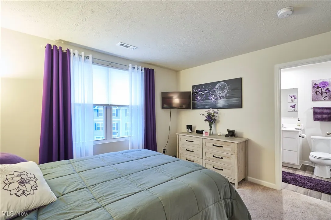 Bedroom with light carpet, a textured ceiling, and ensuite bath