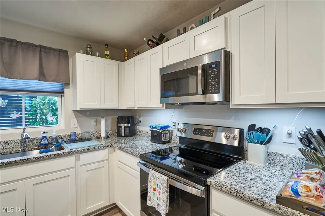 Kitchen featuring appliances with stainless steel finishes, white cabinetry, and light stone counters