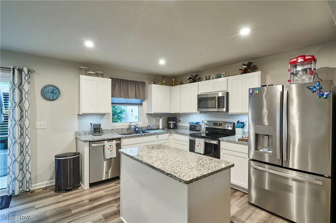 Kitchen with appliances with stainless steel finishes, light wood finished floors, white cabinetry, light stone counters, and recessed lighting