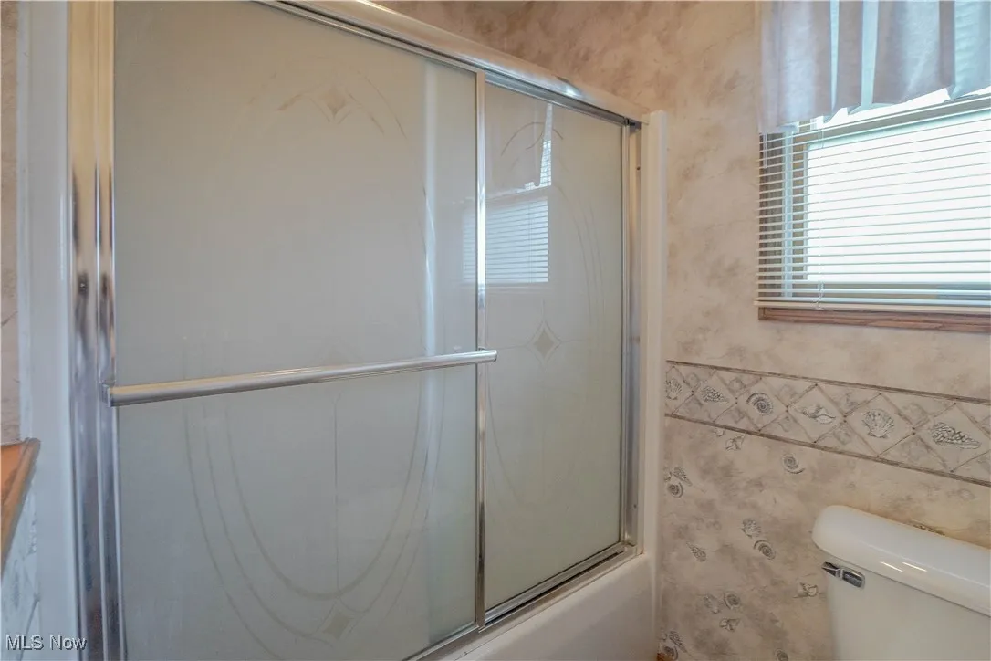 Bathroom with bath / shower combo with glass door and tile walls