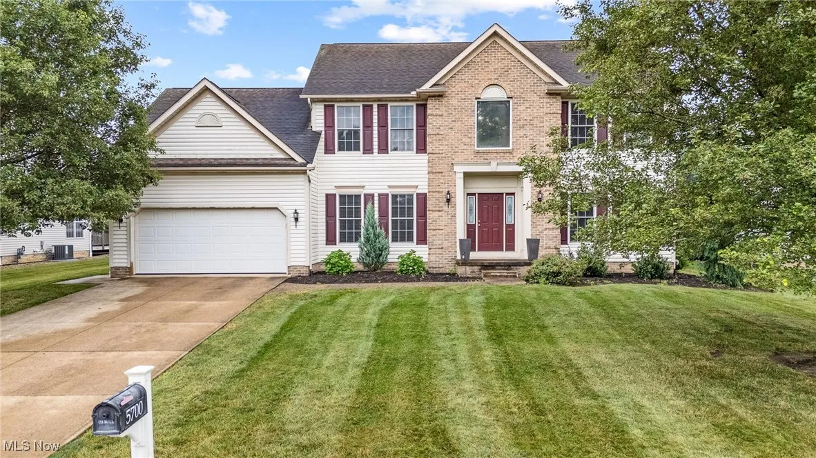 Colonial home with a garage, driveway, a front yard, roof with shingles, vinyl and brick exterior