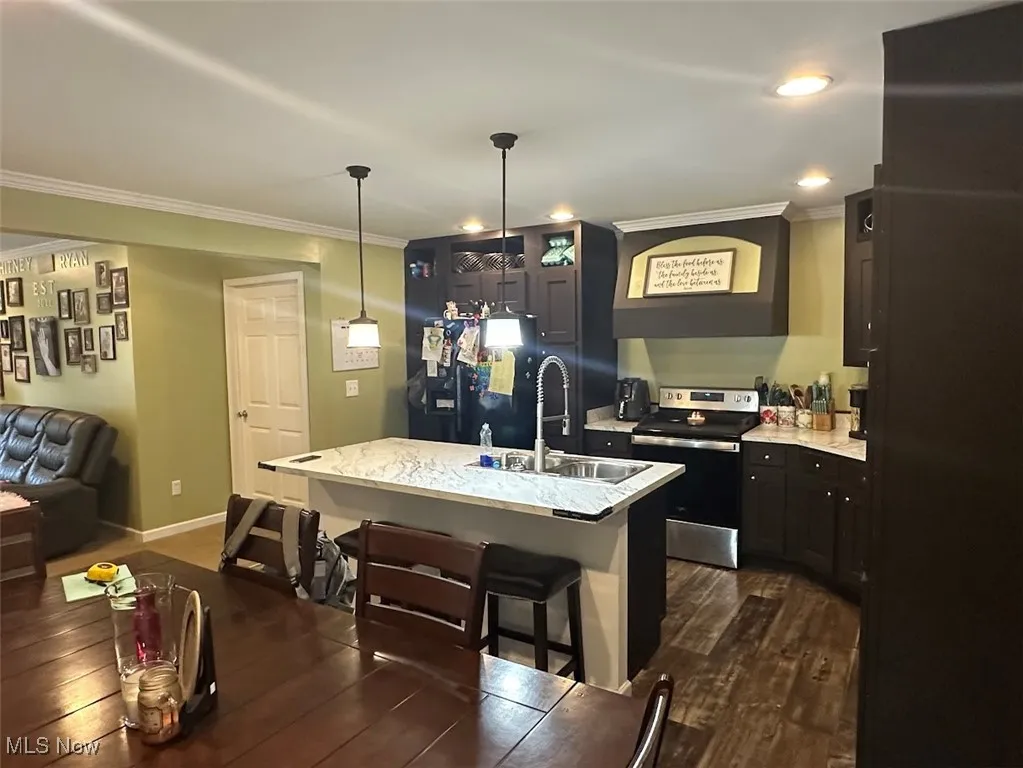 Kitchen featuring stainless steel electric range, ornamental molding, a breakfast bar area, freestanding refrigerator, and dark wood finished floors