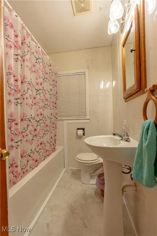 Full bathroom featuring toilet and shower / bath combination with curtain