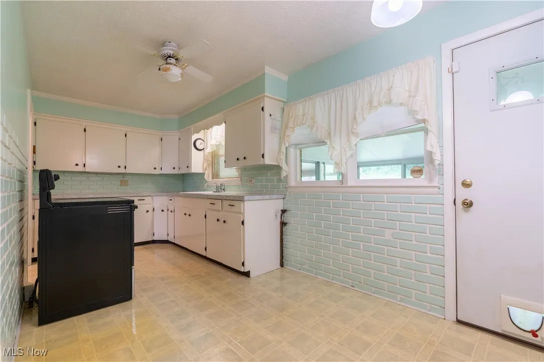 Kitchen featuring light countertops, stove, light flooring, ceiling fan, and backsplash