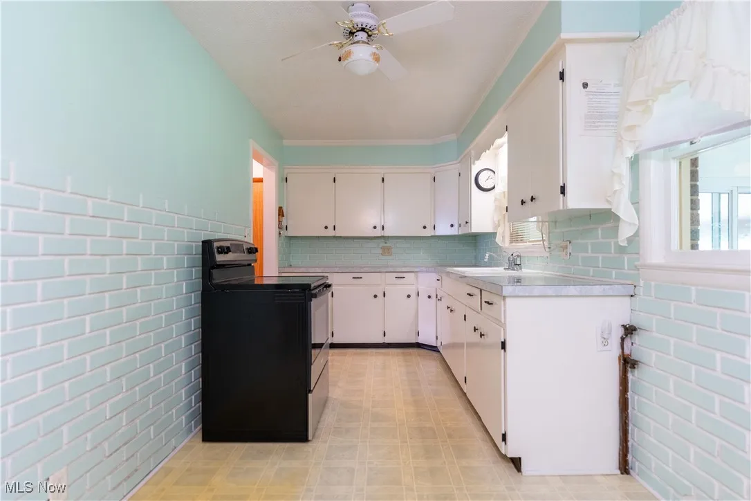 Kitchen with black range with electric stovetop, a ceiling fan, light countertops, light floors, and white cabinetry