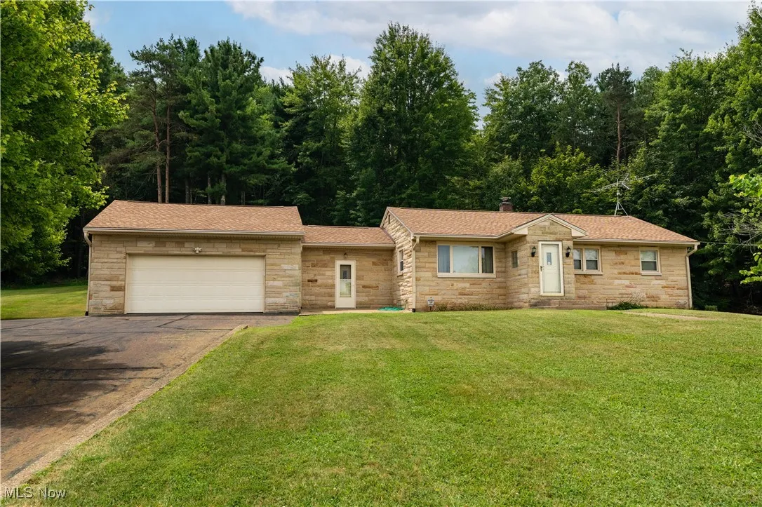 Single story home featuring stone siding, driveway, a garage, and roof with shingles