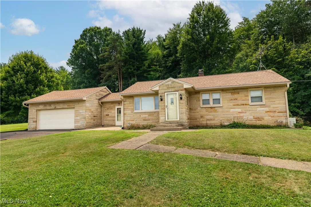 Ranch-style home featuring driveway, stone siding, a garage, and roof with shingles