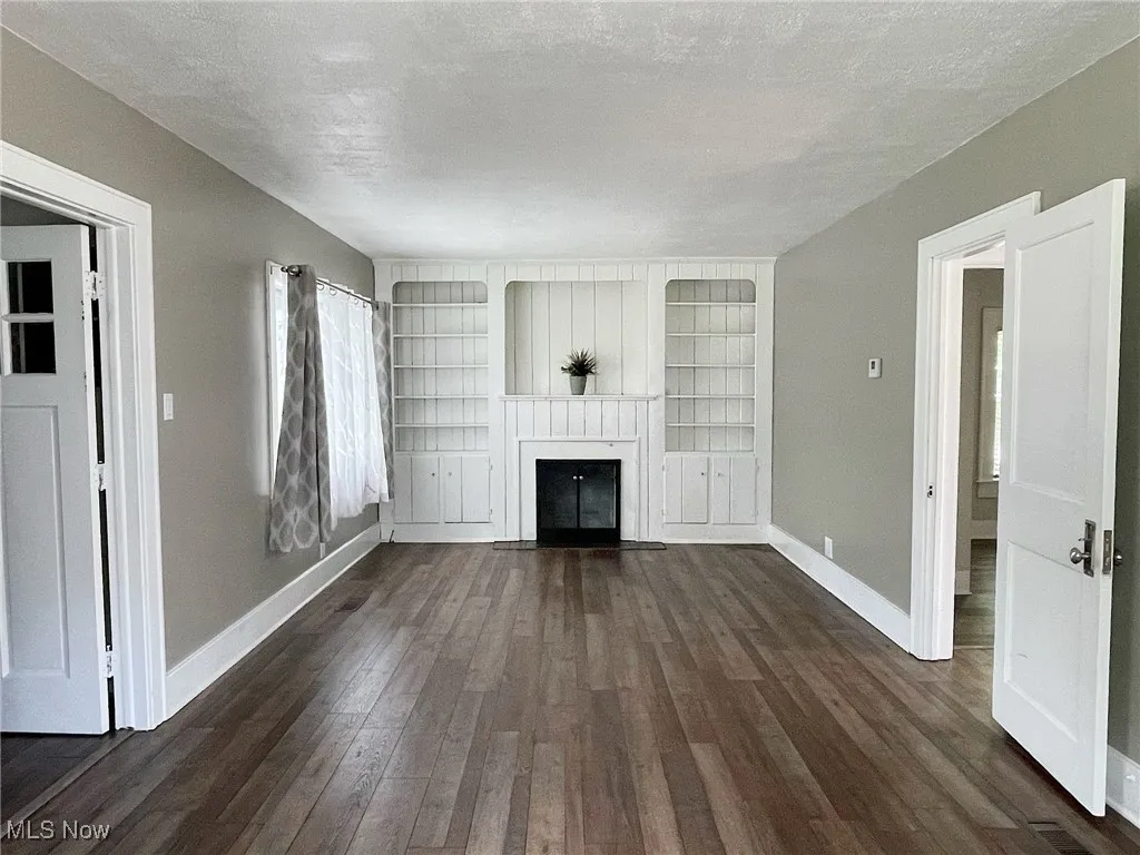 Bright living room with woodburning fireplace with flush hearth, laminate flooring, a textured ceiling, and built in shelves