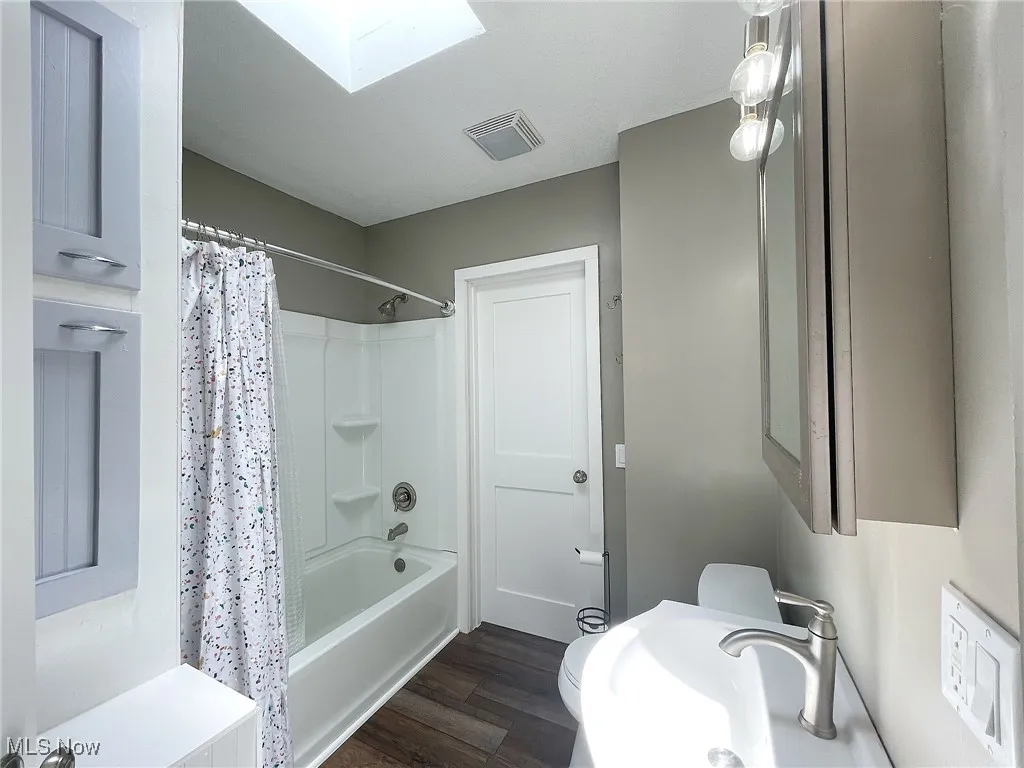 Bathroom with laminate flooring, shower / tub combo, and skylight