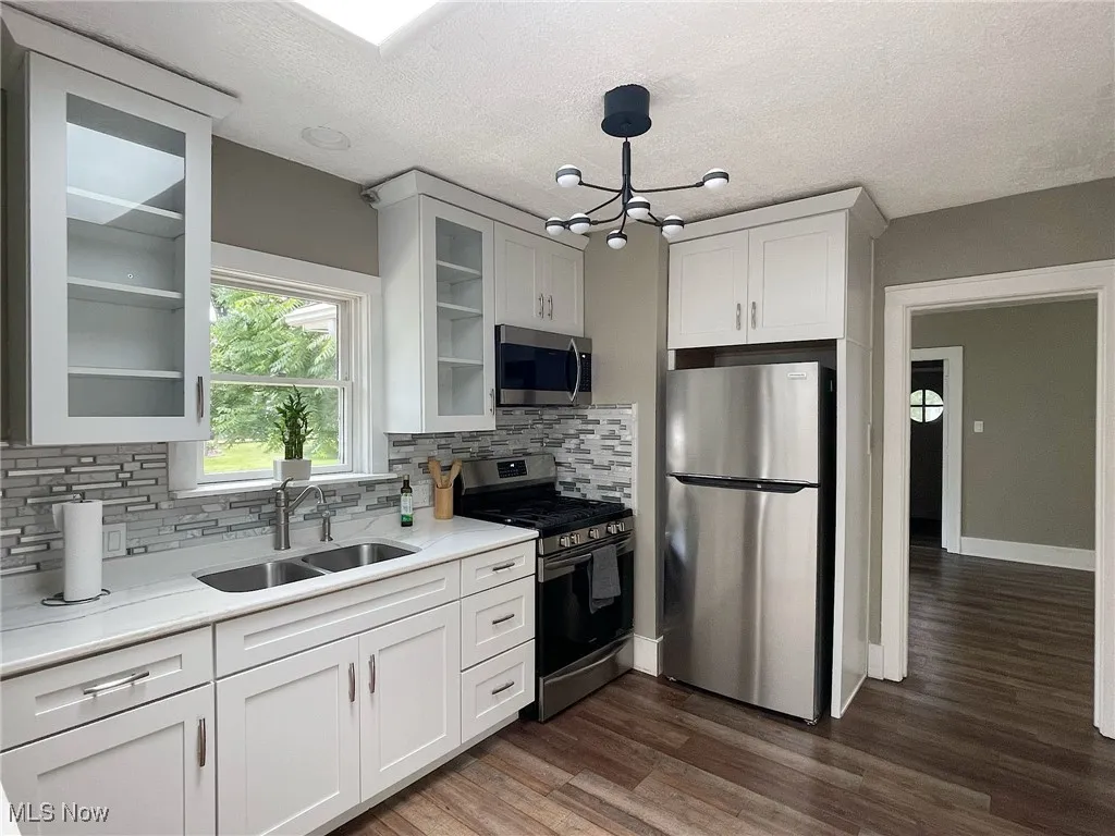 Kitchen featuring appliances with stainless steel finishes, a chandelier, light countertops, decorative backsplash, and glass insert cabinets