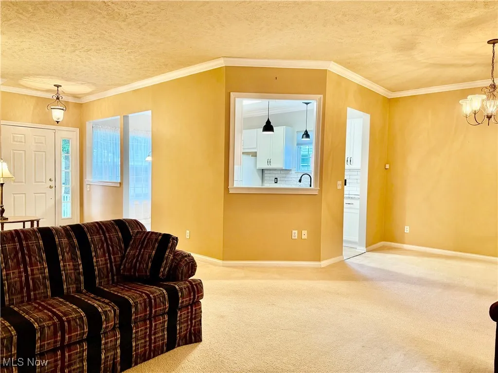 Carpeted living area with a textured ceiling, a chandelier, and ornamental molding