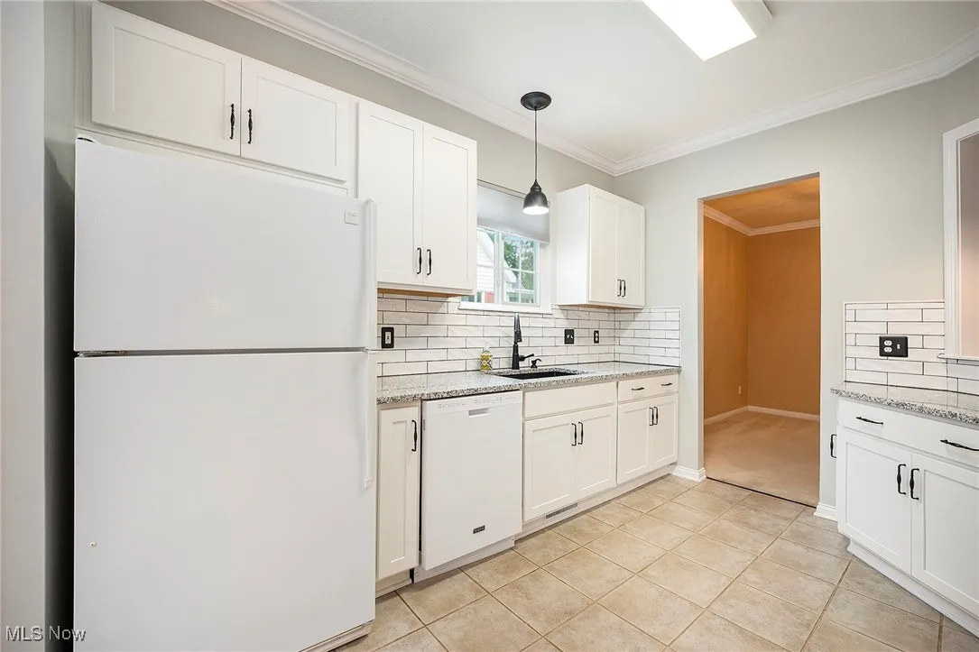 Kitchen with white appliances, decorative backsplash, white cabinets, light tile ceramic floors, and light stone counters