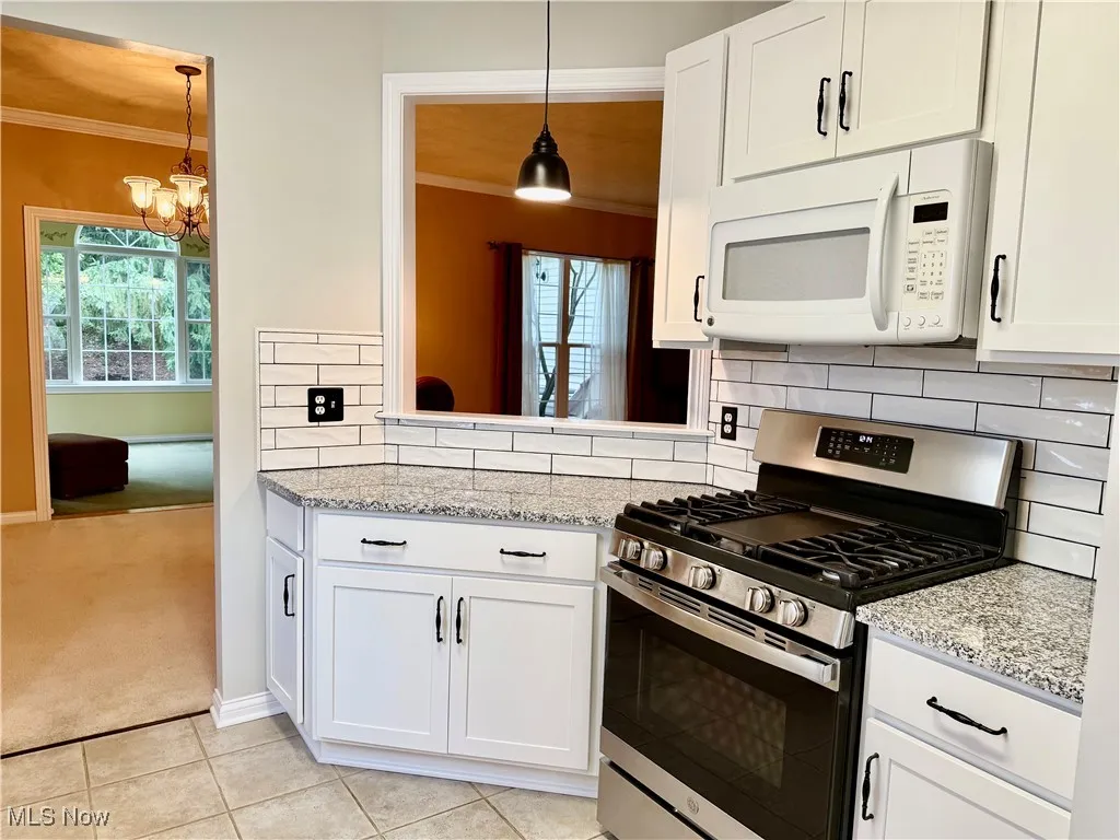 Kitchen featuring gas range, white microwave, a chandelier, crown molding, and light colored carpet
