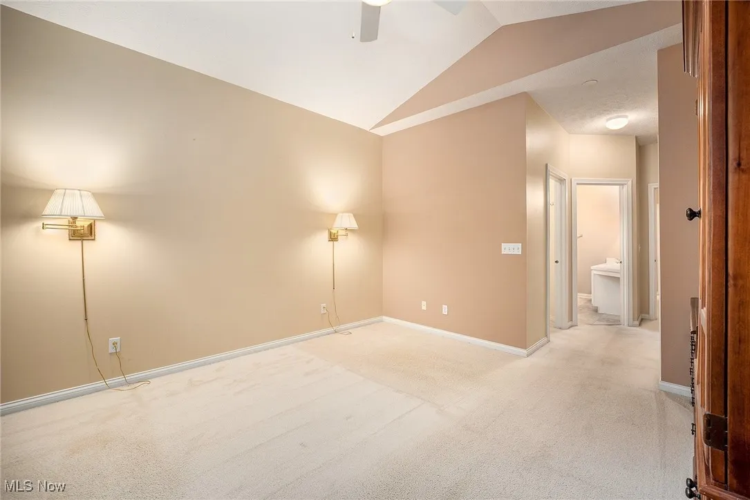 Empty room with lofted ceiling, a ceiling fan, and light carpet