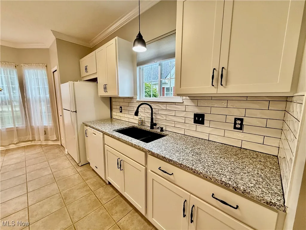Kitchen featuring ornamental molding, decorative backsplash, light stone counters, white appliances, and light tile ceramic floors