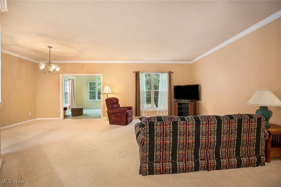 Carpeted living area with a chandelier and ornamental molding