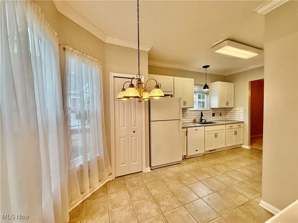 Kitchen featuring white appliances, backsplash, light tile ceramic flooring, white cabinets, and ornamental molding