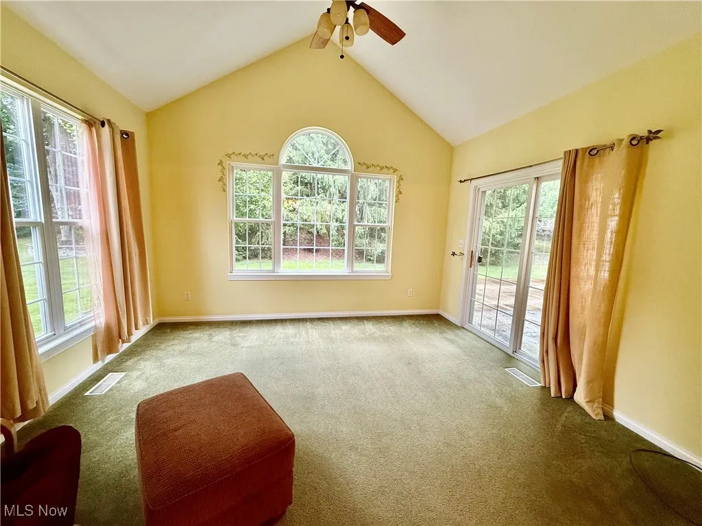 Carpeted empty room featuring plenty of natural light, ceiling fan, and lofted ceiling