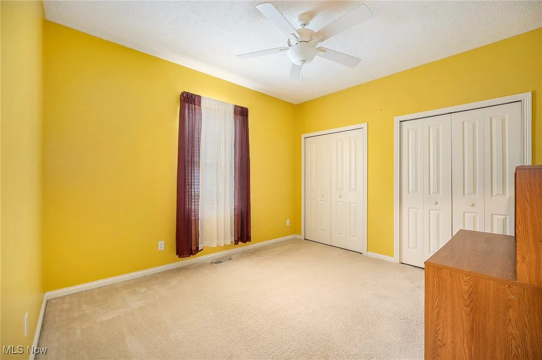 Unfurnished bedroom with light carpet, two closets, and a ceiling fan