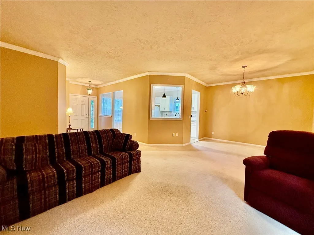 Carpeted living area with a chandelier, crown molding, and a textured ceiling