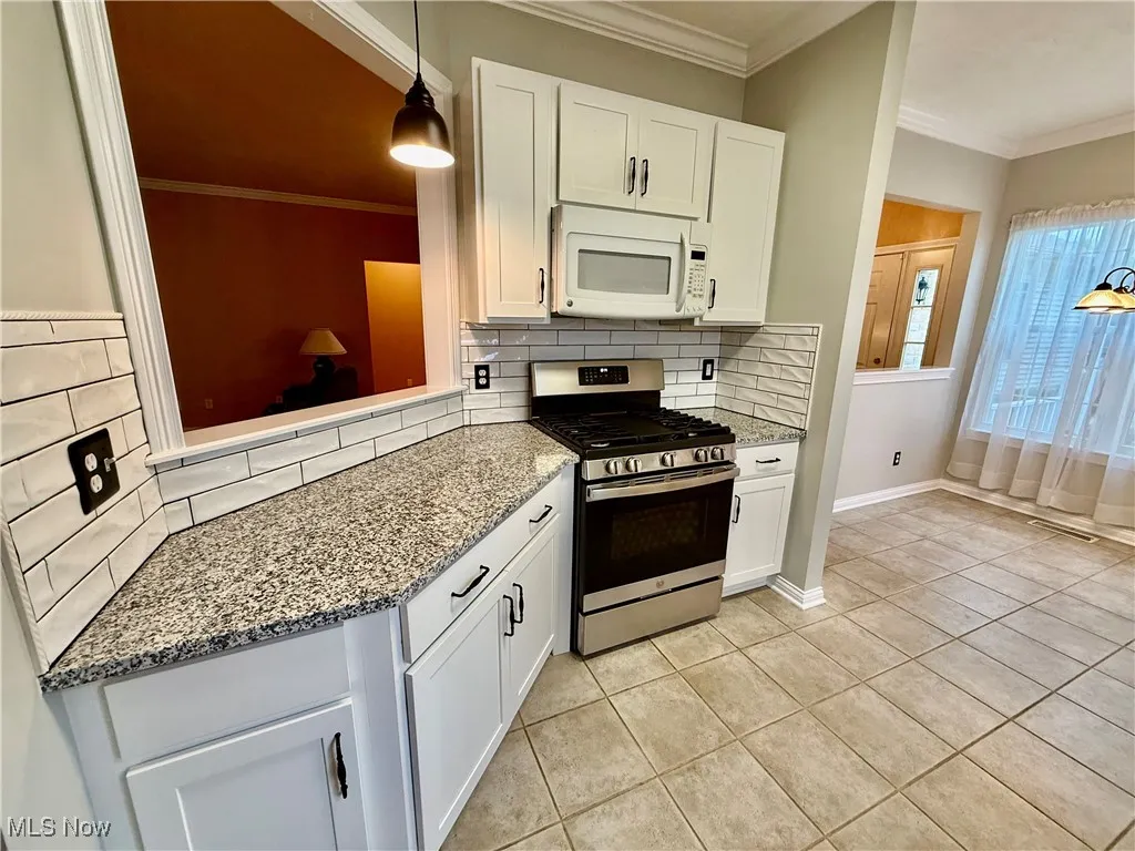 Kitchen with stainless steel range with gas stovetop, white microwave, backsplash, light  counters, and white cabinetry
