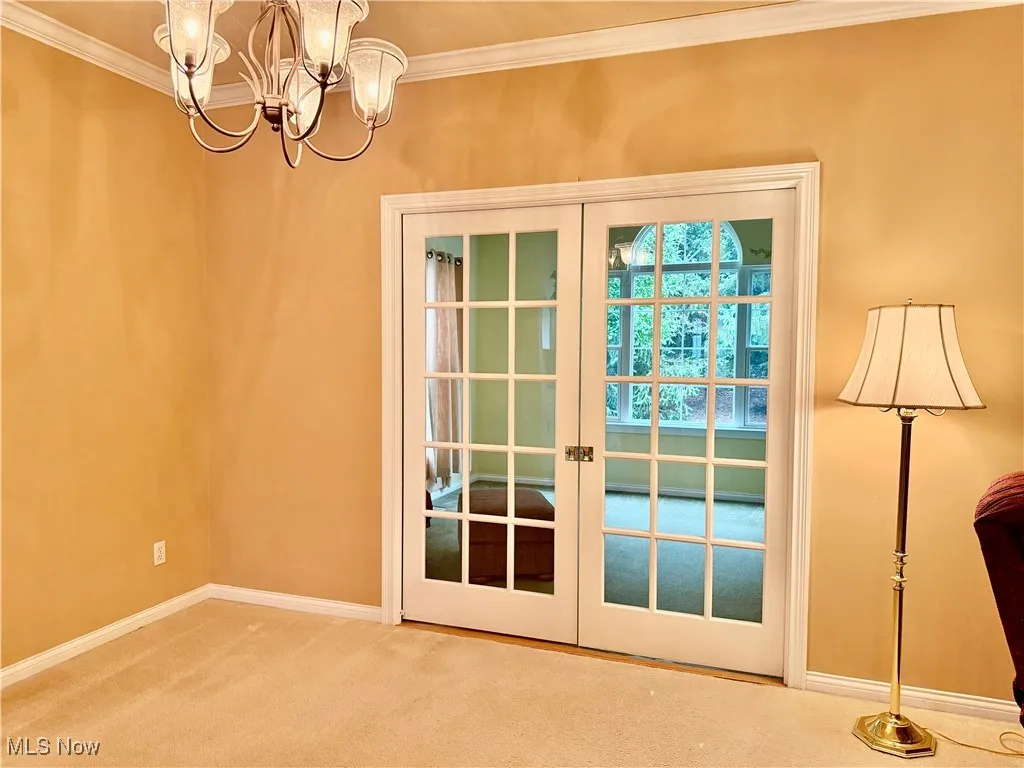 Doorway to sunroom with a chandelier, carpet, ornamental molding, and french doors