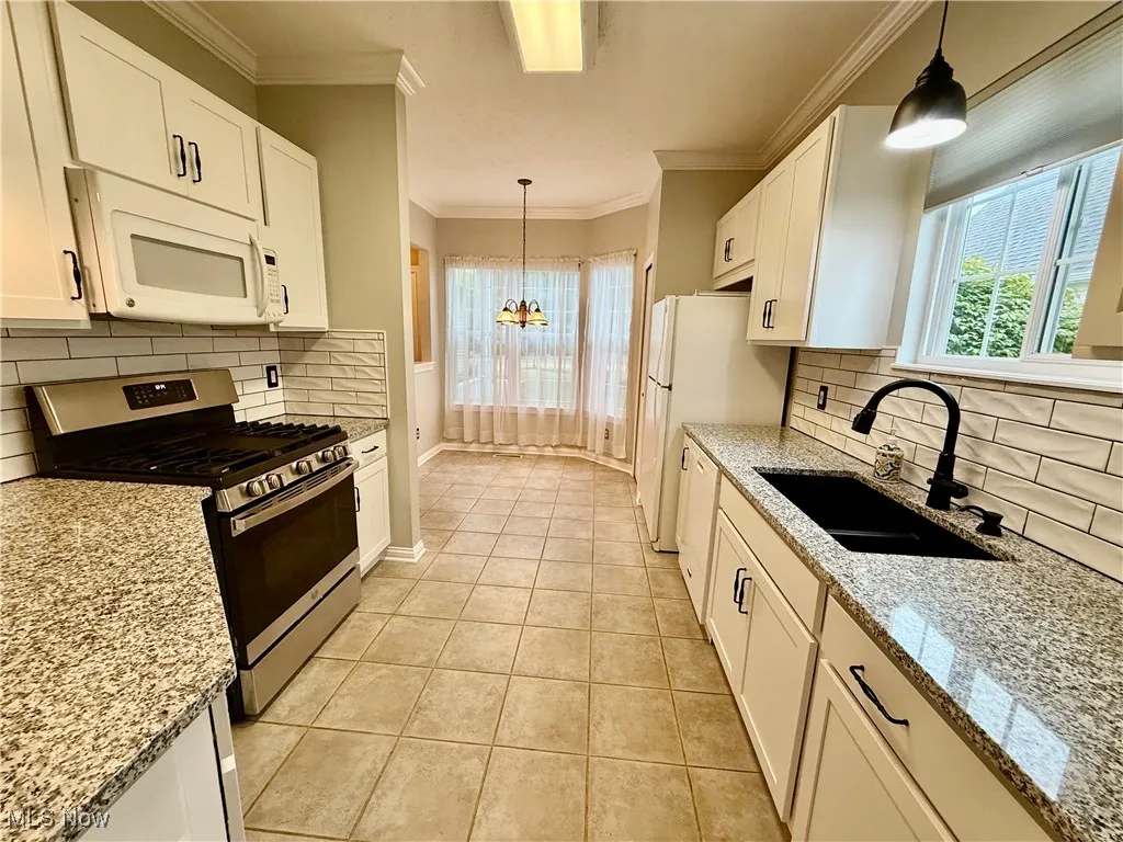Kitchen with white appliances, a chandelier, light tile patterned floors, white cabinets, and decorative backsplash