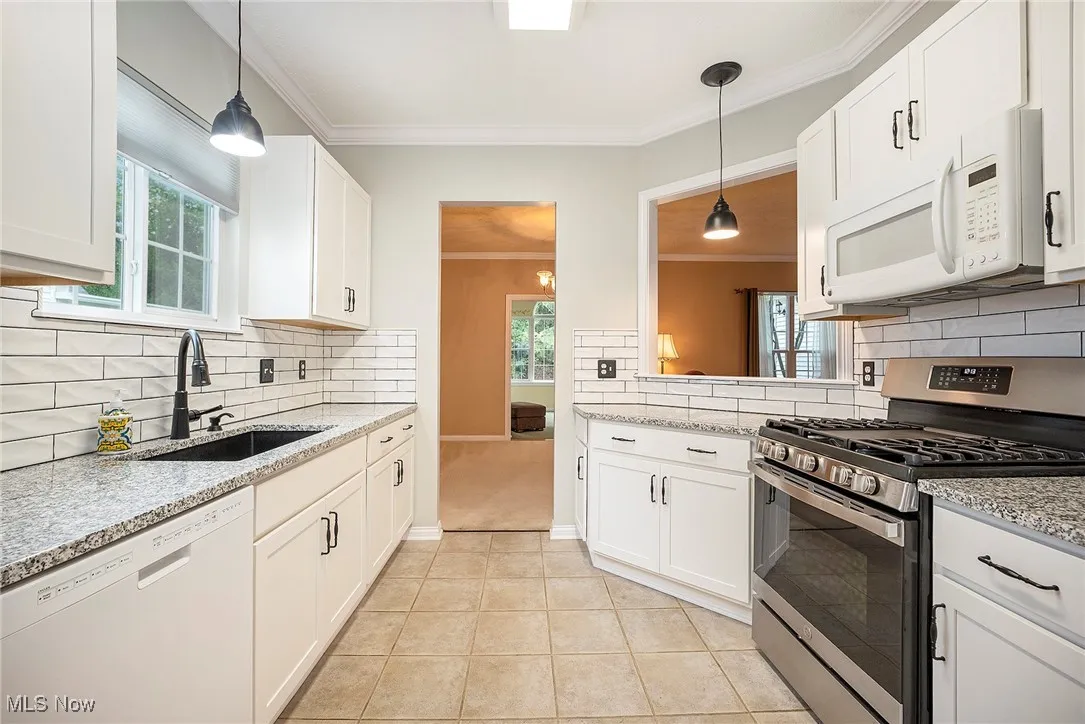 Kitchen with white appliances, ornamental molding, backsplash, decorative light fixtures, and light tile ceramic floors