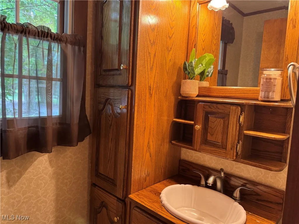 Bathroom featuring wallpapered walls, vanity, and ornamental molding
