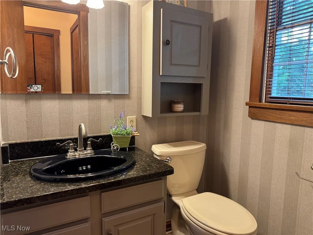  bathroom with granite countertop, wallpapered walls and vanity& shower