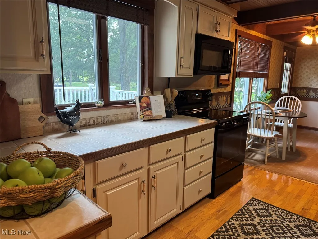 Kitchen featuring black appliances, tile countertops, healthy amount of natural light, light wood finished floors, and beam ceiling