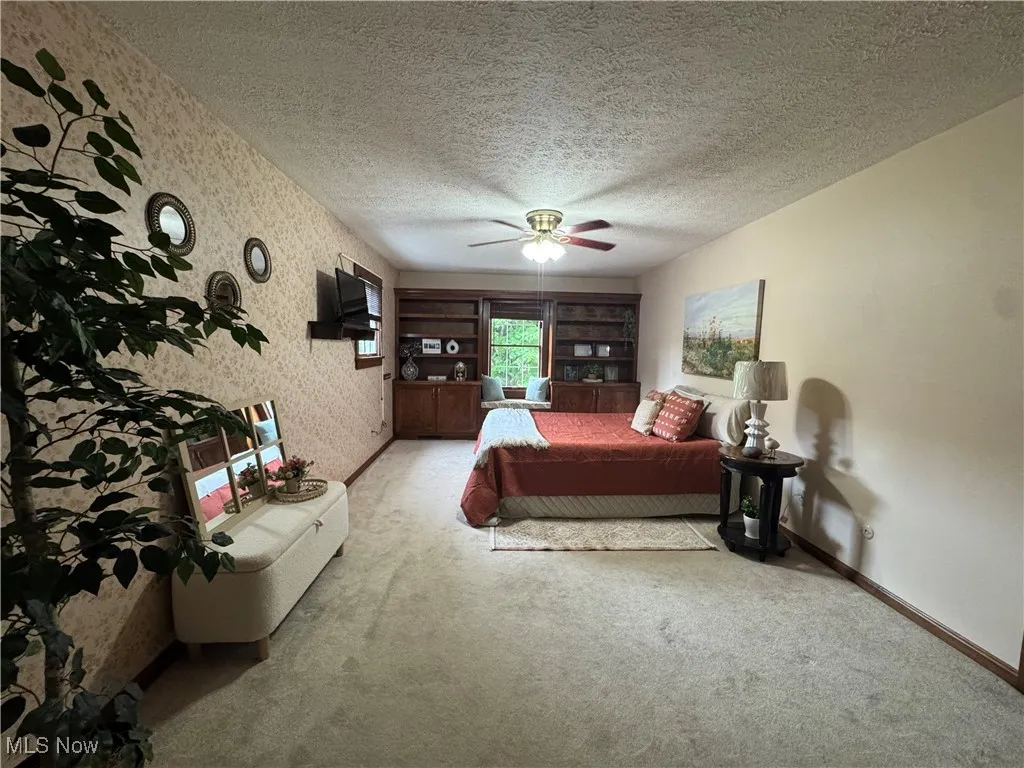 Bedroom featuring wallpapered walls, carpet floors, a ceiling fan, and a textured ceiling