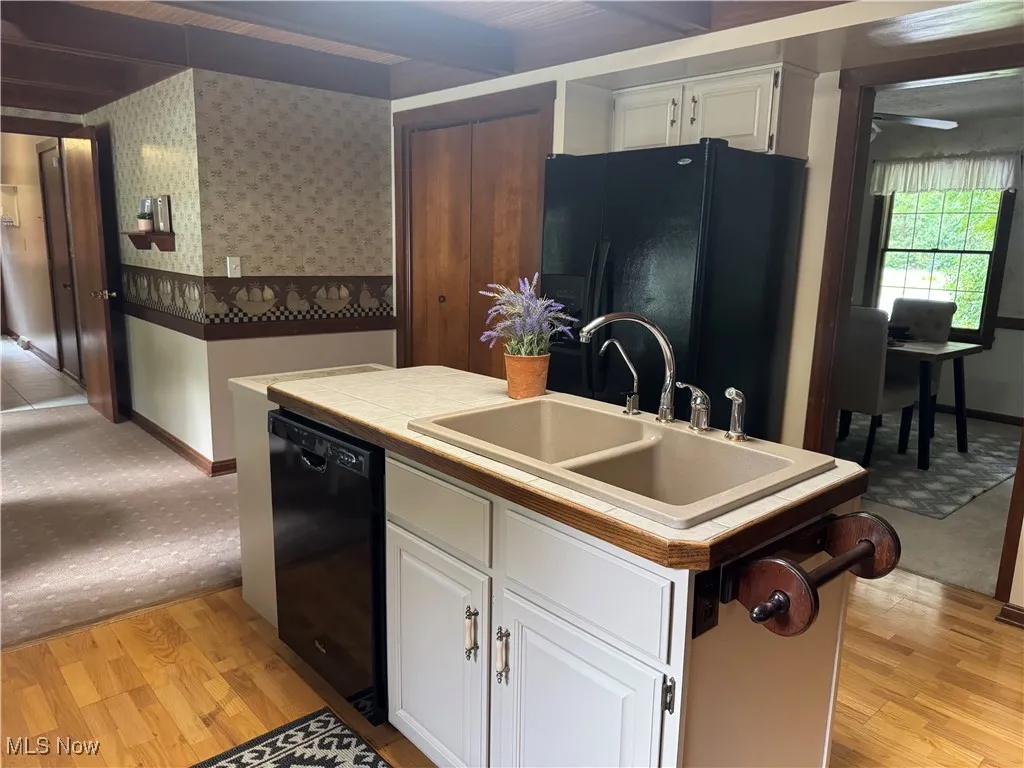 Kitchen with black appliances, white cabinets, light wood-type flooring, wallpapered walls, and tile counters