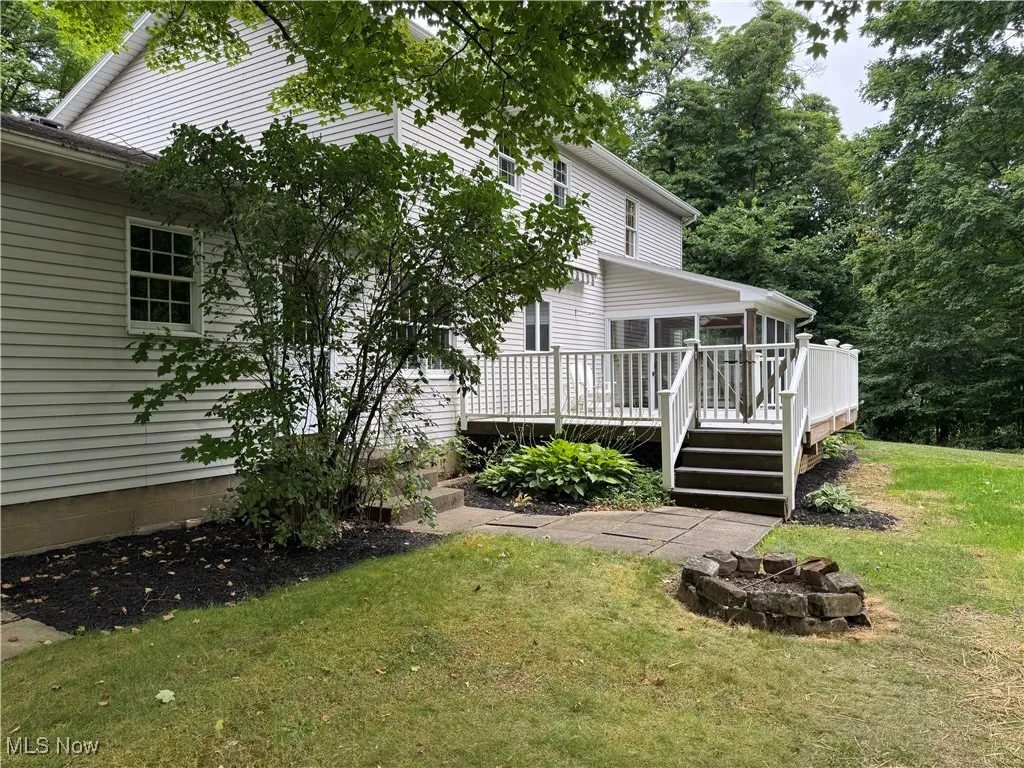 Back of property with a sunroom, a fire pit, a wooden deck, and a yard