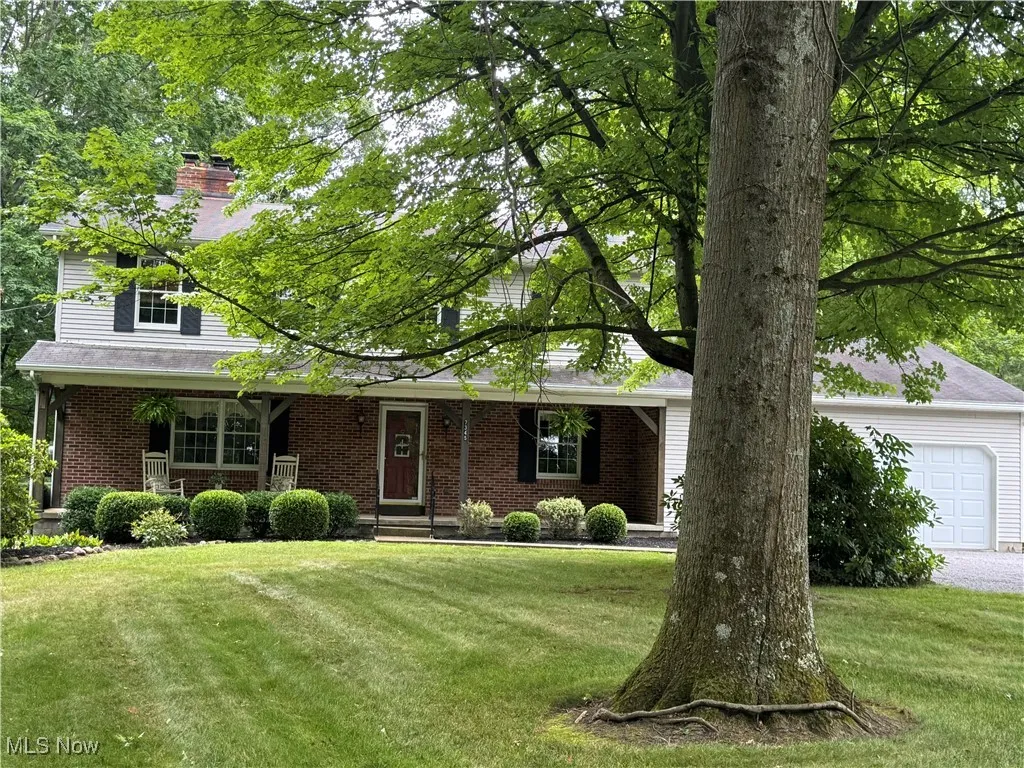 View of front of home featuring brick siding, a front lawn, a chimney, and covered porch