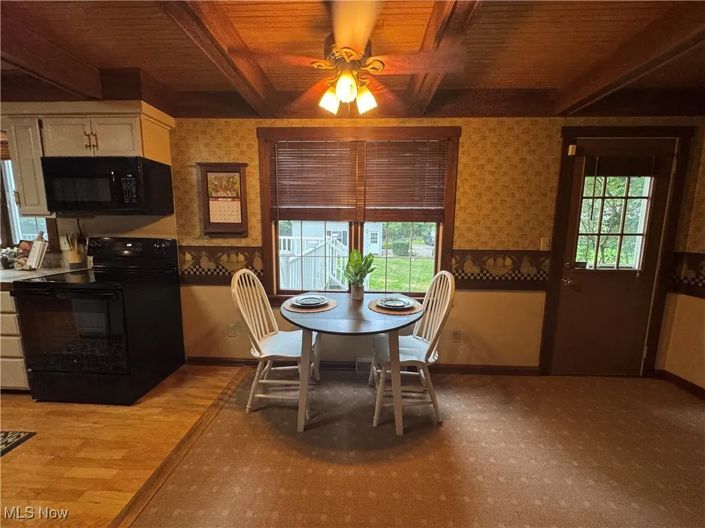 Dining area featuring wallpapered walls, ceiling fan, and a wooden ceiling with exposed beams