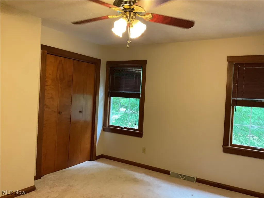 Unfurnished bedroom featuring a closet, light colored carpet, and a ceiling fan