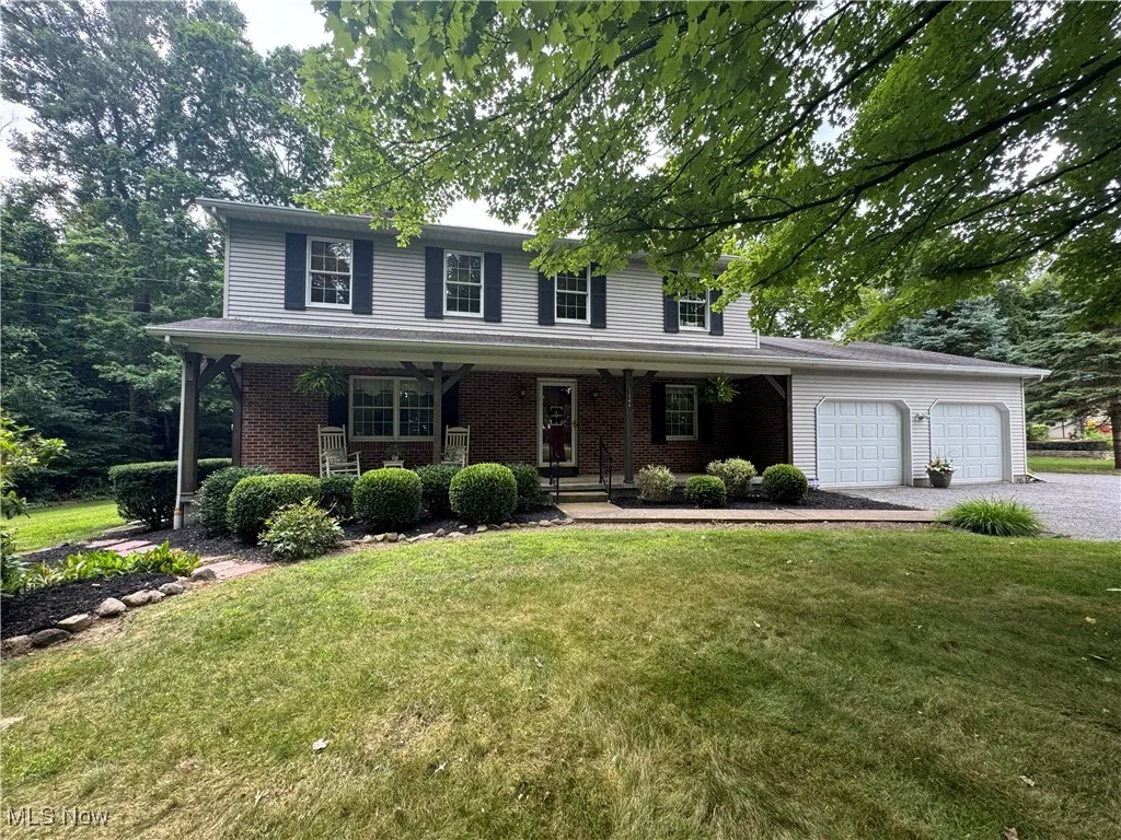 Traditional home featuring brick siding, a garage, covered porch, and a front yard